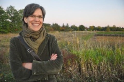 Sarah Martin with her arms crossed and a scarf around her neck outside in a field
