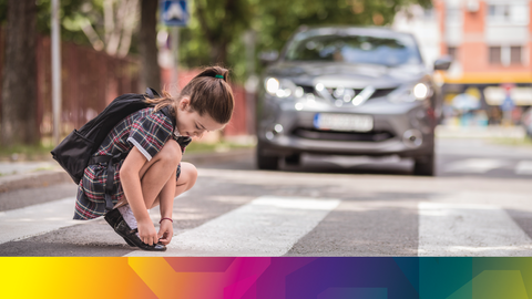 A child bending down to tie thier shoes with a car menancing them