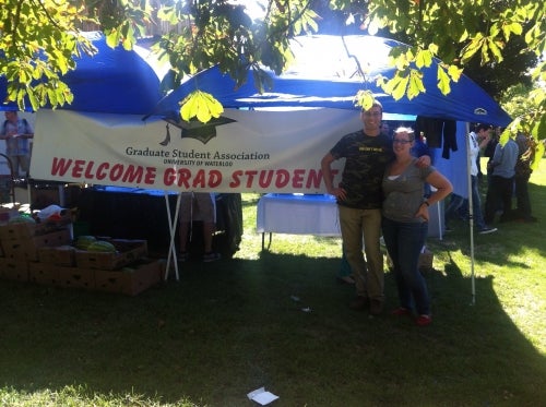 Banner welcoming graduate students with two students at an orientation tent
