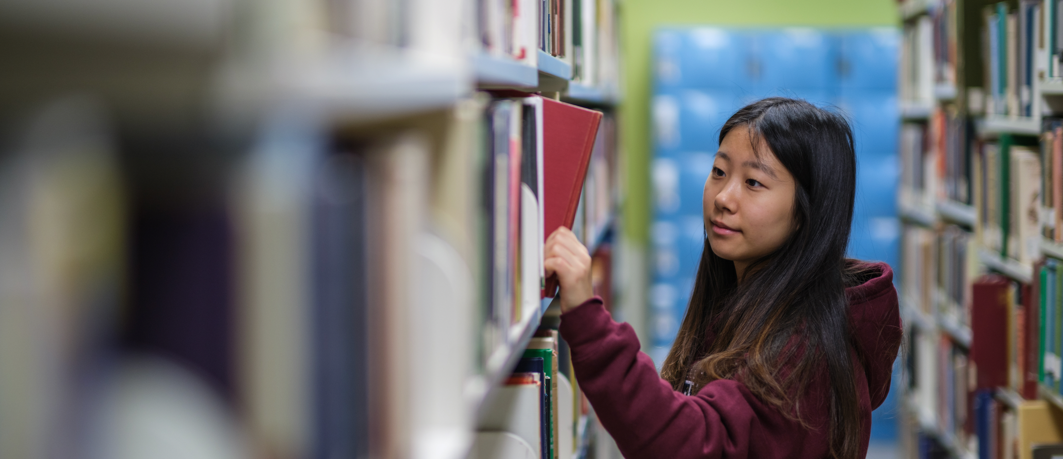 student in library looking at book on shelf