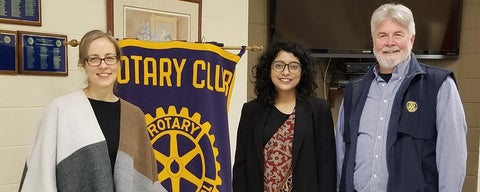 Sidra (middle) stands beside a Rotary club banner, with two administrators