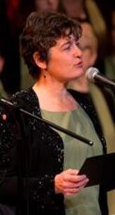 Jane Ramseyer Miller speaking at microphone at choral event
