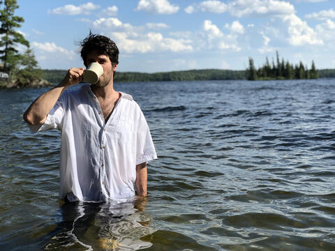 Jesse Matas standing waist-deep in lake drinking out of mug