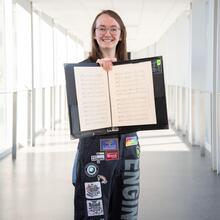 Student standing holding open book of music scores