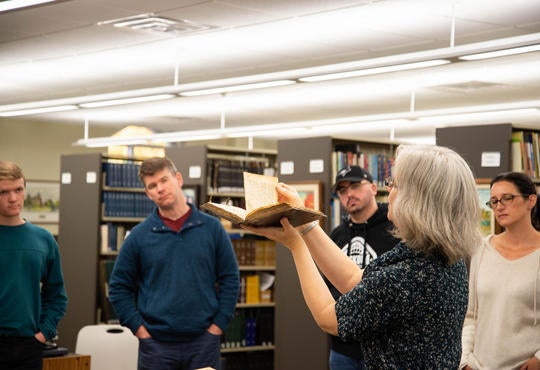 Archivist-Librarian Laureen Harder-Gissing holds up book from the Mennonite Archives of Ontario for David Neufeld's class to see