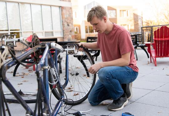 Liam Armstrong crouched beside his bike as he repairs its tire.