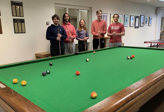 Four students standing around pool table