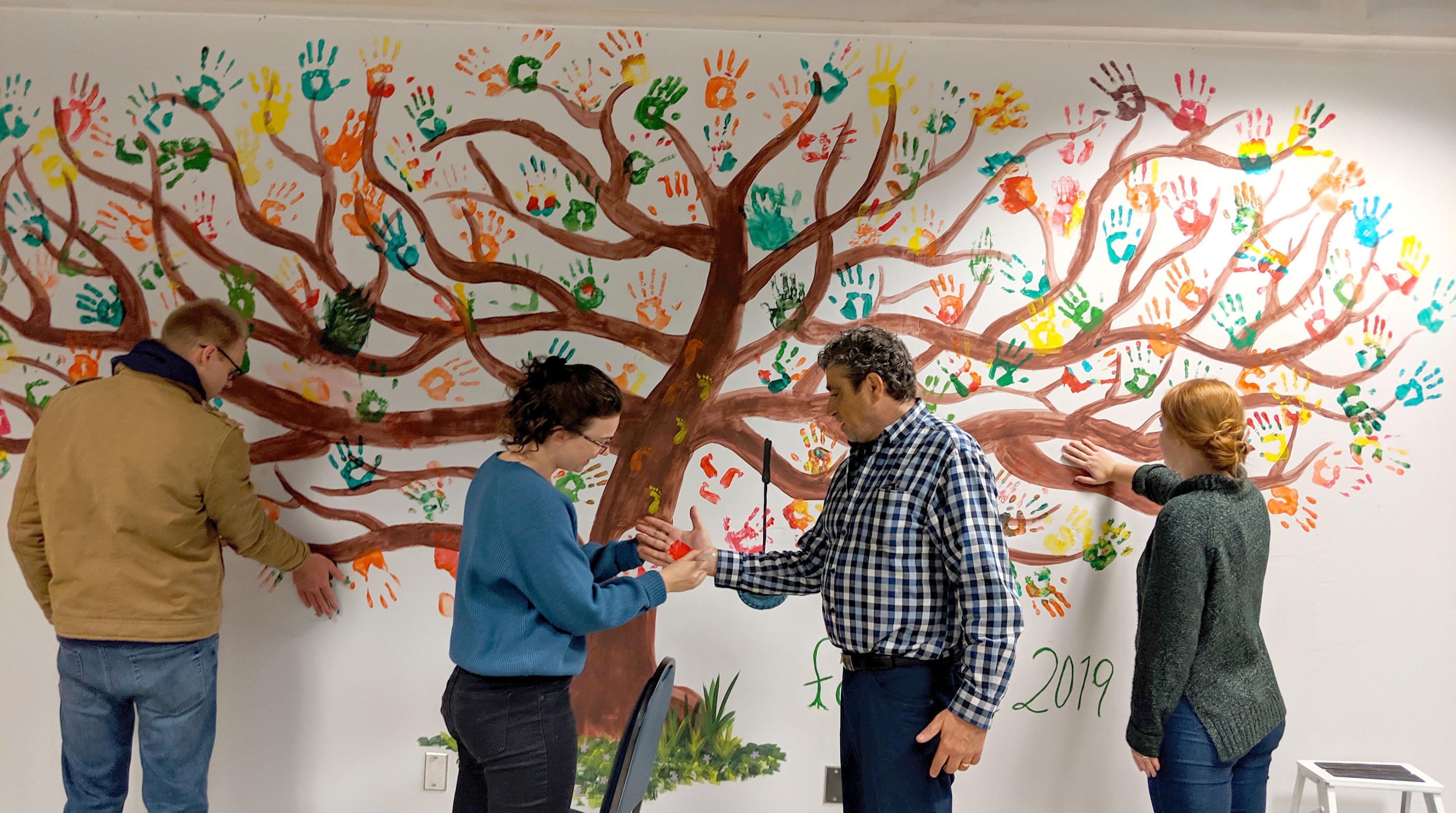 Staff and students adding their handprints to the painted tree in the dining room