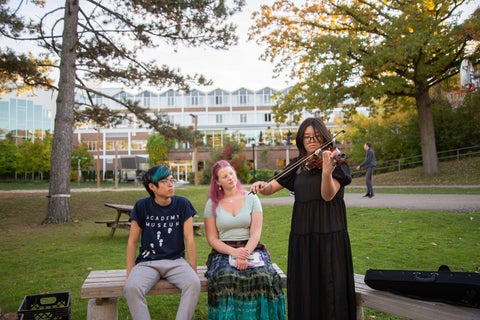 Darley Dau playing violin outside Grebel with two students listening