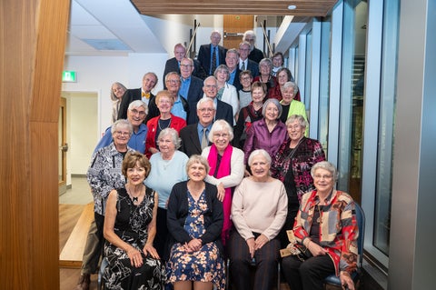 a group of 25 alumni from the 1960's sit for a group photo in the Grebel dining room