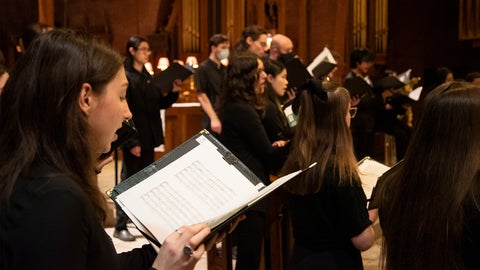 A close up of a woman singing in a choir. She holds a folder with sheet music.