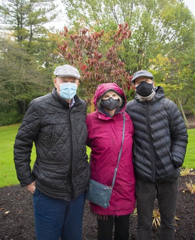 three people wearing face masks standing in front of a baby tree 