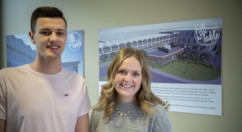 two students standing by a sign with a mockup of a green roof 