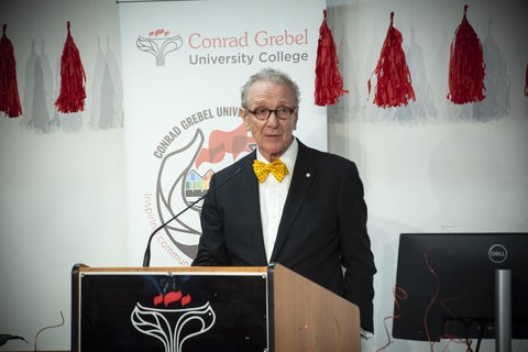 alumni speaking at podium in front of Grebel banner and red tassle decorations