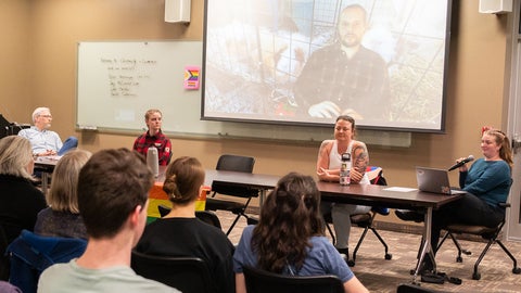 A panel of four people plus someone on a screen behind them