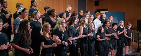 A group of young adults dressed in black, perform as a choir on stage