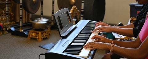 a view of an electric piano with two people practicing. 