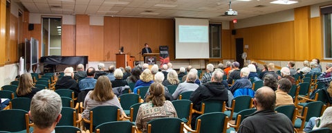 a crowd sits and listens to a lecture in the great hall