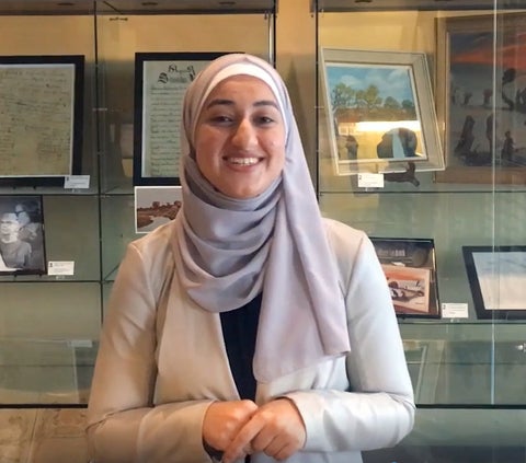 boushrah standing in front of a glass cabinet full of frames 