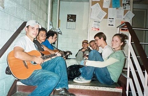 Caleb Boyd playing guitar with a group of students siting in a stairway 