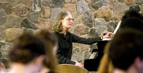 Catherine Robertson sits at a piano in a full Grebel chapel.