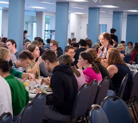 Students gathered at large table eating and talking at Grebel Community Supper