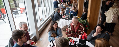 An overhead shot of families gathered in the Grebel dining room after convocation, around circular tables.
