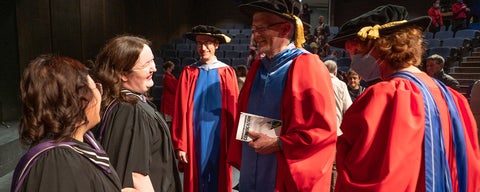 Two recently graduated grad students laugh with three professors in their red and blue PhD gowns. 