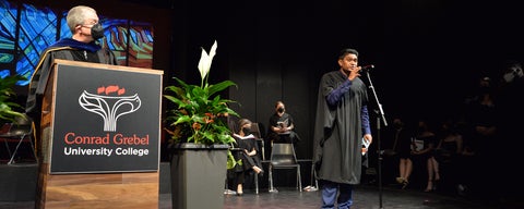 a grad student speaks at a microphone during convocation celebrations