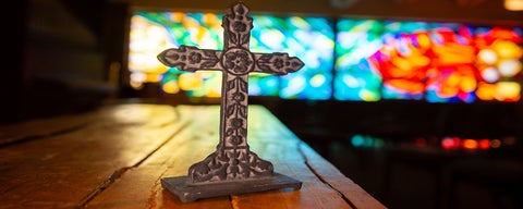 A cross on a table with stained glass windows in the background