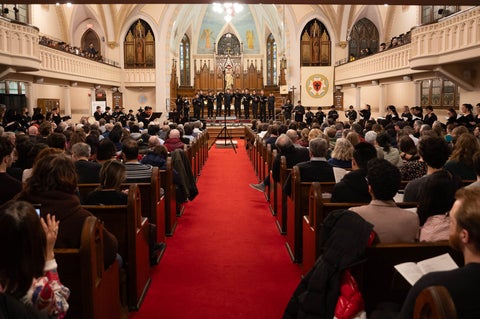 looking down the aisle of a church sanctuary, pews filled with people listening to a choir sing on stage