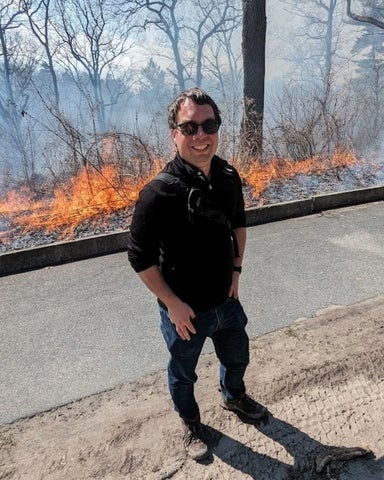 Man in sunglasses on the side of the road in front of a wildfire