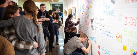 Students crowd around a large wall in the Grebel Gallery where they can write and draw