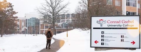 A student walking down a snowy path outside the Grebel building