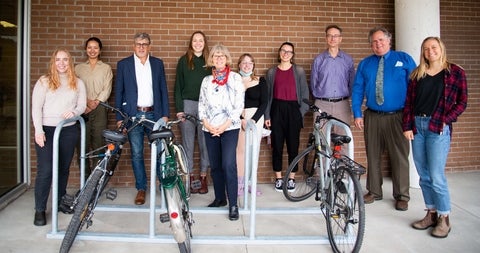 A group of grebel staff, students, and faculty stand beside a bike rack outfront of Grebel's brick wall, They represent the green team.