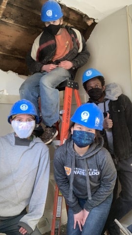 four studnets posing in a construction site wearing blue hard hats