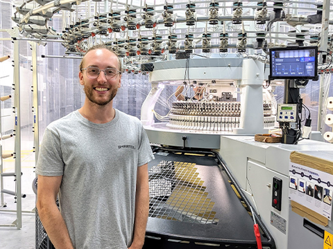 Jared stands in front of an industrial knitting machine.