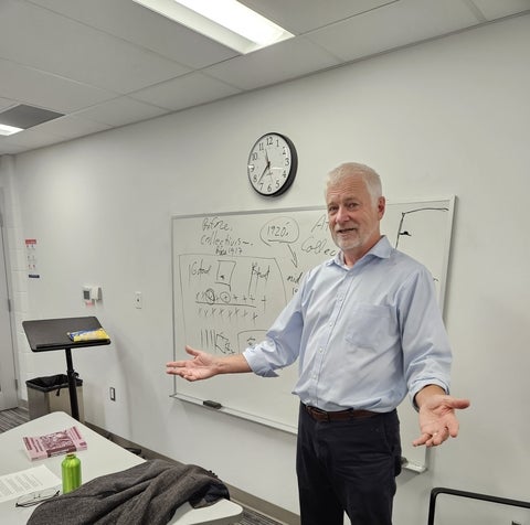 Len Friesen standing in front of whiteboard with open arms 