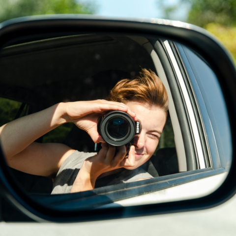 Gwendolyn Friesen taking a photo of themsleves with a camera in a car side mirror
