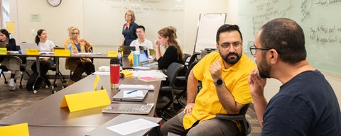 Two masters students talk to each other during a class.