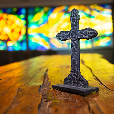 A cross in the chapel with stain glass in the background