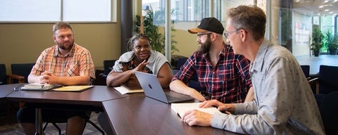 Three MTS students talk with each other during a class, with a professor