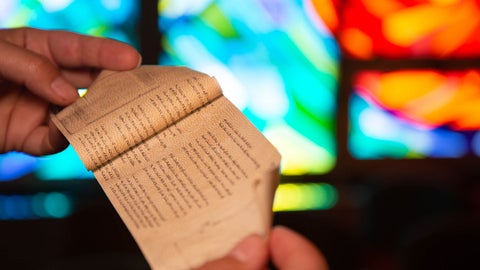 hand holding small scriptural paper with stained glass in the background