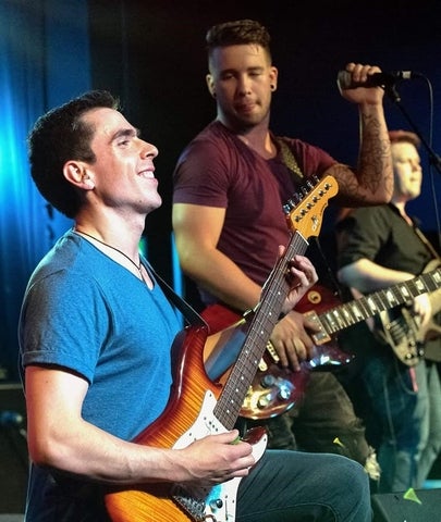 Nick playing a guitar with other bandmates behind him