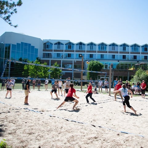 Staff running towards airborn volleyball on Grebel's sandy volleyball court at staff versus student volleyball game