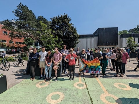 students standing in Arts quad holding pride flag quilt