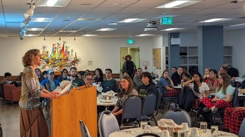Jane Kuepfer speaking at podium in Cafeteria