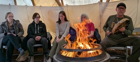 people gathered around a fire while someone plays a hand drum