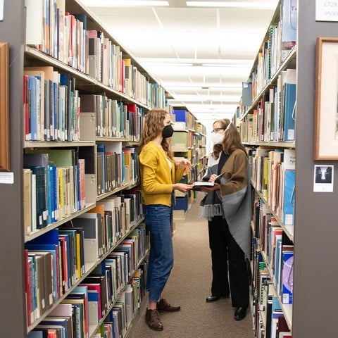 A student and professor discuss over a book between library shelves