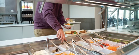 a student reaches for a metal tong in the salad bar area of the kitchen. 